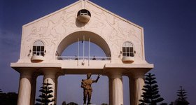 Title: I was visiting The Gambia, on the western tip of Africa. The Gambia is a true banana republic. Here is the triumphal arch and statue of himself that the President erected after his successful coup d'état.